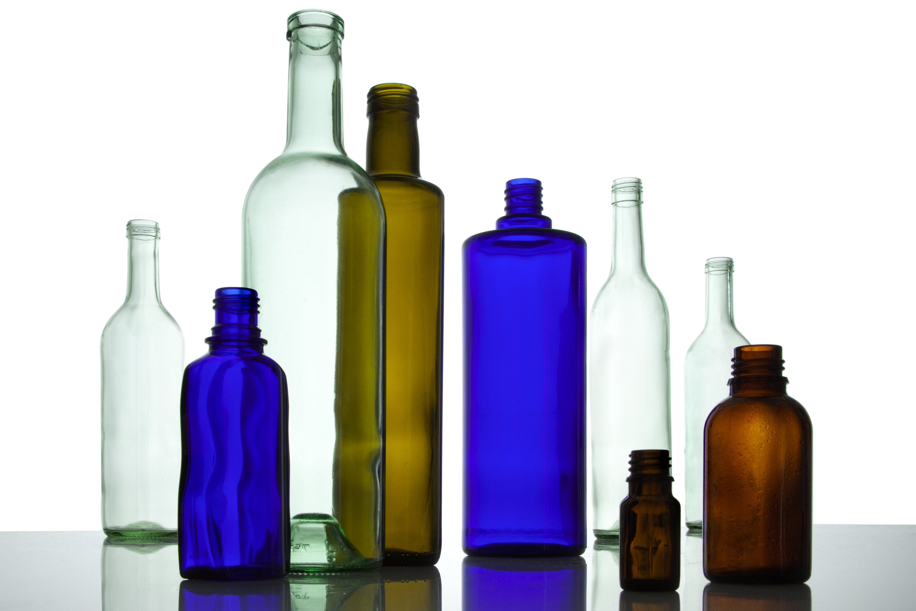 Mehrere leere Glasflaschen in verschiedenen Farben stehen neben- und hintereinander.