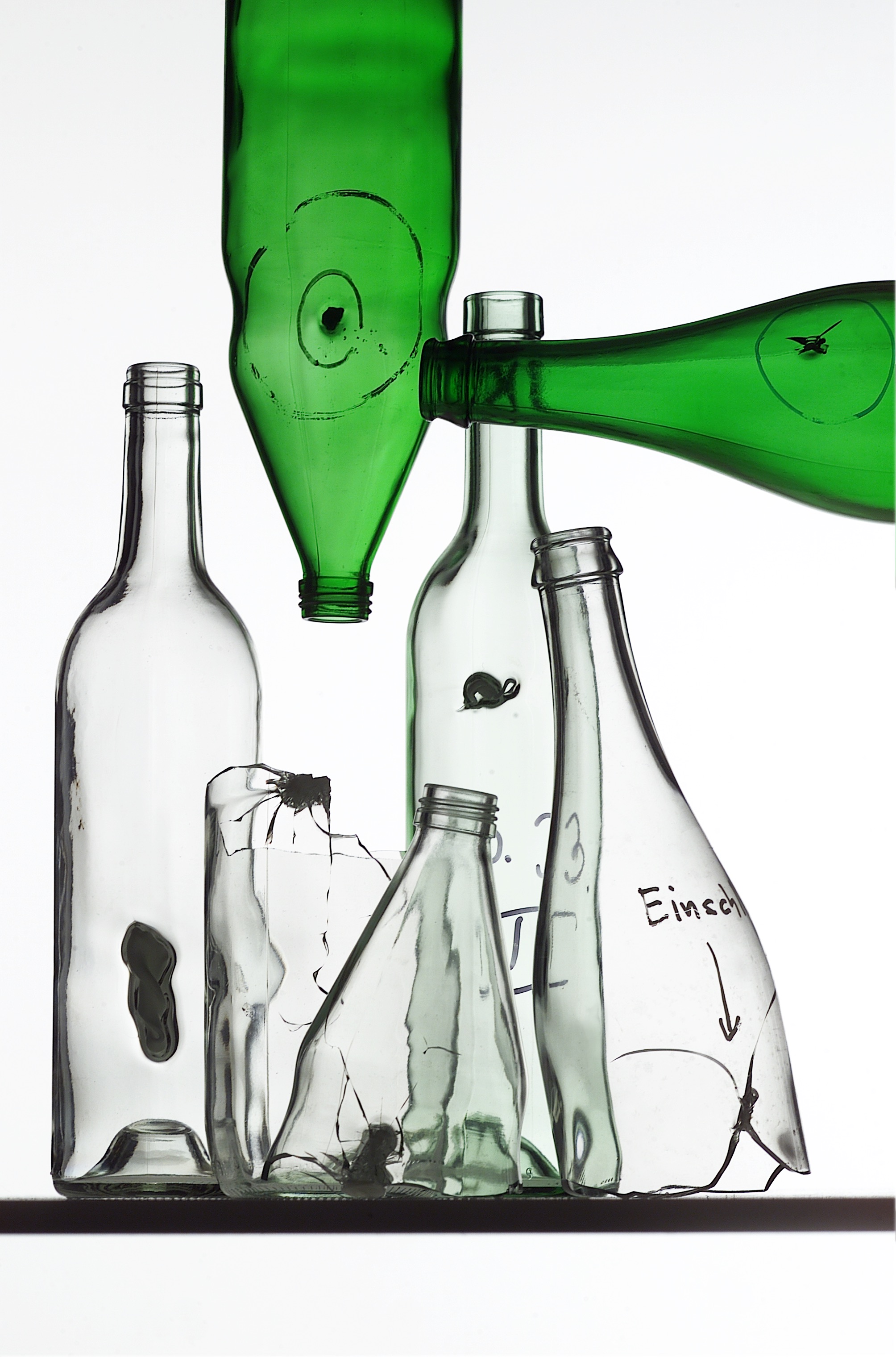 Mehrere durchsichtige Flaschen und zwei grüne, die alle fehlerhaft sind, da sie sogenannte Einschlüsse aus anderen Materialien enthalten.