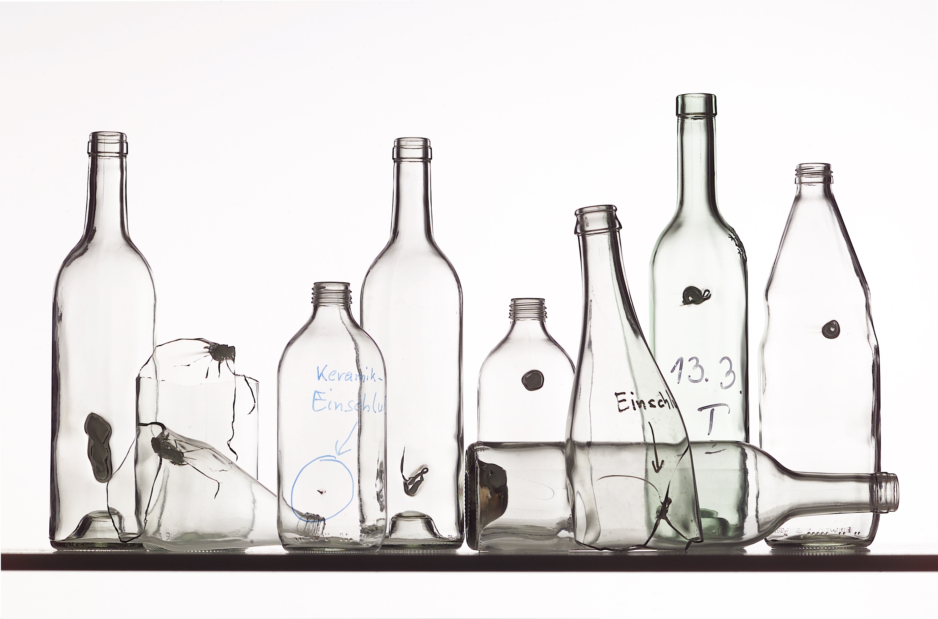 Mehrere durchsichtige Flaschen, die alle fehlerhaft sind, da sie sogenannte Einschlüsse aus anderen Materialien enthalten.