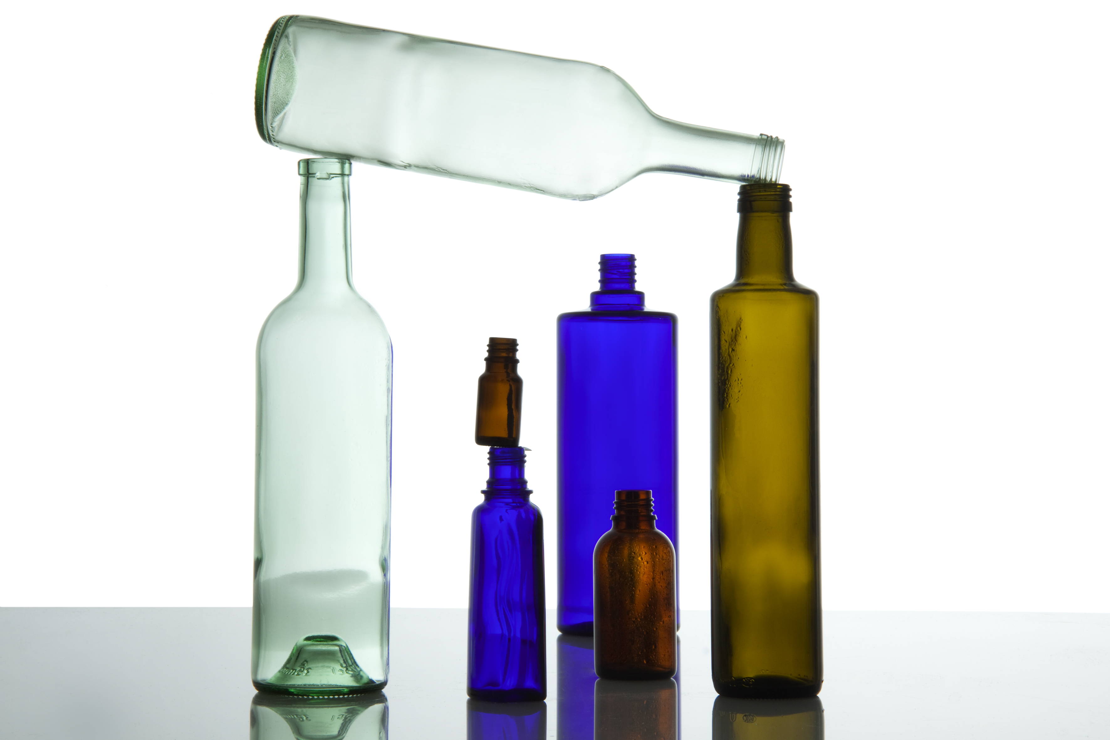 Mehrere farbige Glasverpackungen tragen eine hellgrüne leere Glasflasche, die quer über den anderen liegt.