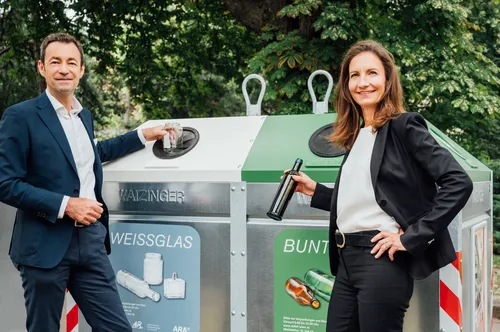 Zwei Personen vor Weißglas- und Buntglas-Containern beim Einwerfen von Glasverpackungen.