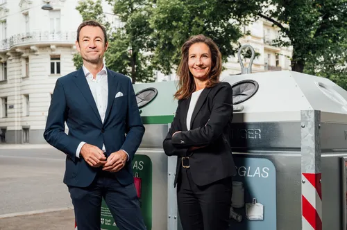 Zwei Personen stehen vor Glascontainern für Weißglas und Buntglas.